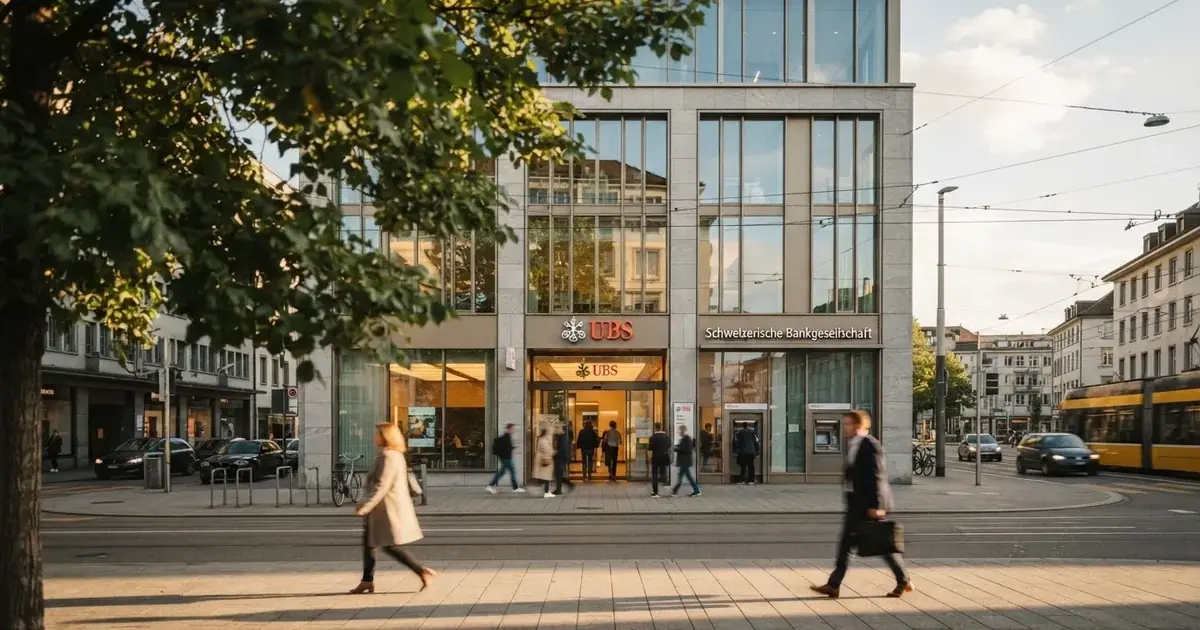 Blick auf eine helle Bankfiliale mit Glasfassade von der Strasse aus, Passanten gehen unscharf vorbei.